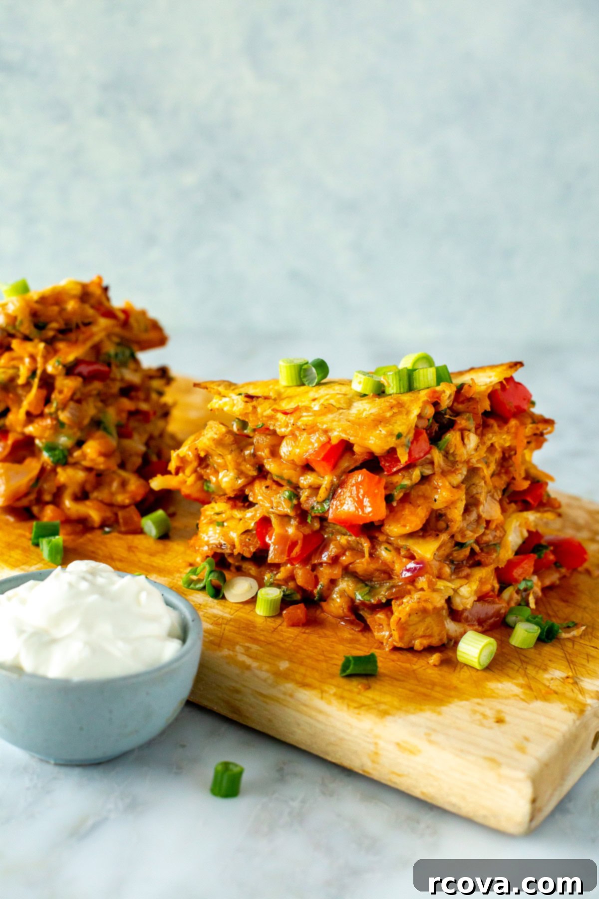 Your New Favorite Chicken Quesadilla 9 Stacks of cut chicken quesadillas on a wooden cutting board with sour cream on the side.
