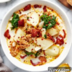 One Pot Restaurant-Style Zuppa Toscana 9 A comforting bowl of Zuppa Toscana soup, rich with creamy broth, sausage, potatoes, and kale, garnished with red chili flakes and a piece of bread.