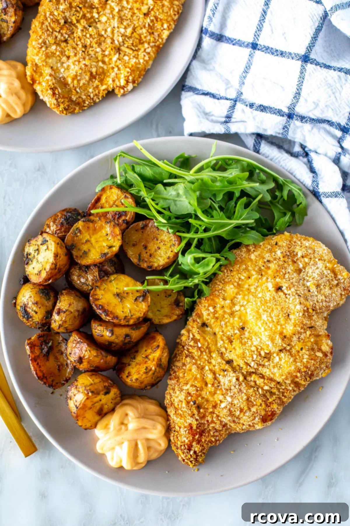 Crispy and Juicy Oven Baked Chicken Cutlets 7 A close-up photograph of a single plate showcasing a golden, crispy chicken cutlet alongside aromatic lemon dill potatoes and a small serving of fresh arugula for a balanced and appetizing meal.