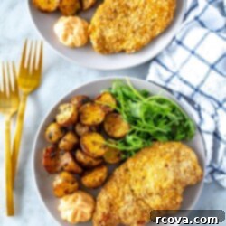 Crispy and Juicy Oven Baked Chicken Cutlets 9 Two plates, each with a chicken cutlet, lemon dill potatoes and a side of arugula.