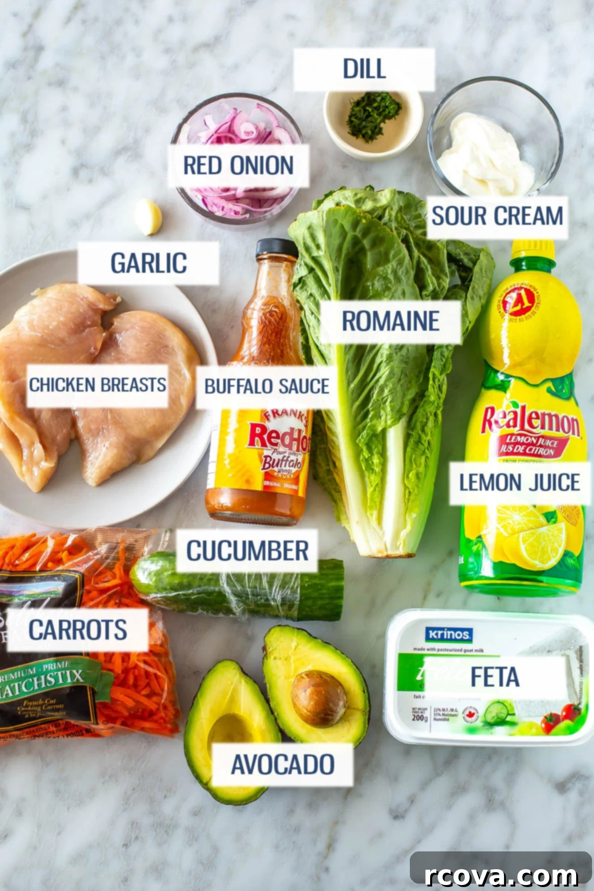Lightened Up Buffalo Chicken Salad 3 Ingredients for buffalo chicken salad laid out: chicken breasts, garlic, red onion, dill, sour cream, carrots, buffalo sauce, romaine lettuce, lemon juice, cucumber, avocado, and feta cheese.