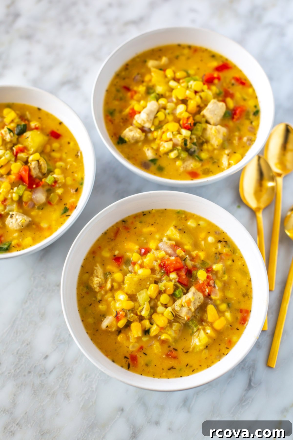 Easy Creamy Chicken Corn Chowder 8 Three bowls of chicken corn chowder with three gold spoons placed next to them, arranged aesthetically.