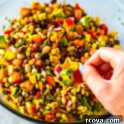 The Only Cowboy Caviar Recipe You'll Ever Need 9 A hand with a tortilla chip scooping up cowboy caviar from a bowl.