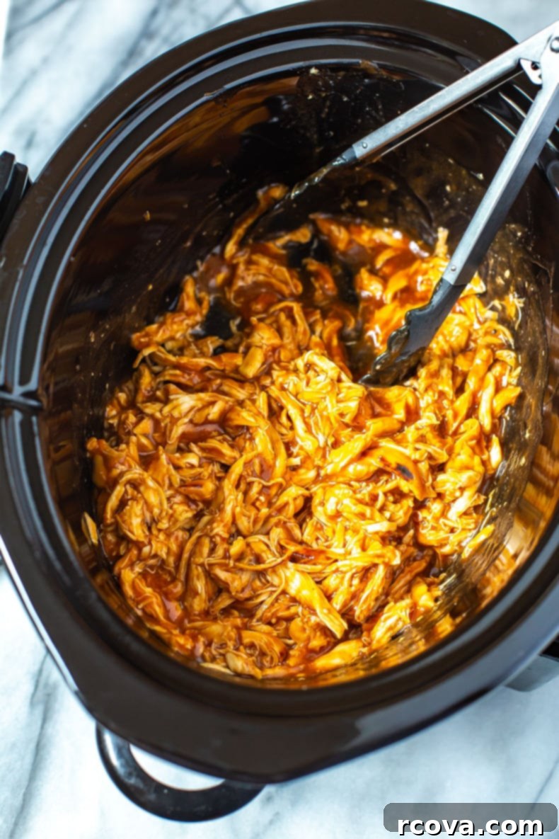 Happy Plates: 24 Healthy Dinners Your Kids Will Devour 16 A close-up shot of a slow cooker filled with shredded BBQ chicken with open tongs inside.