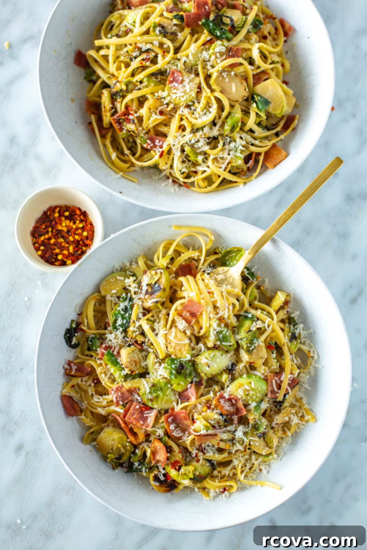 Bacon Brussels Sprouts Creamy Pasta 2 Two bowls of creamy brussels sprouts pasta garnished with chili flakes and fresh Parmesan cheese, with a small bowl of extra chili flakes next to them, ready to be served.