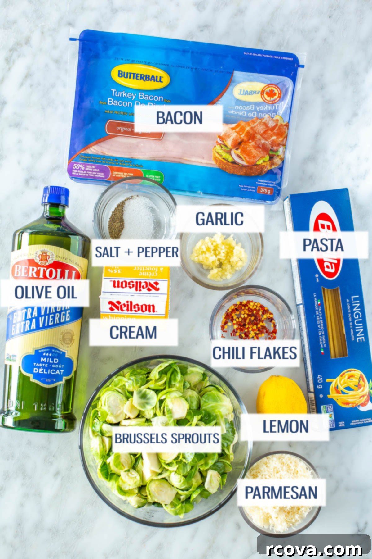 Bacon Brussels Sprouts Creamy Pasta 4 A vibrant flat lay of all the fresh ingredients needed for creamy brussels sprouts pasta: fresh bacon, linguine pasta, olive oil, garlic cloves, salt, pepper, shaved brussels sprouts, chili flakes, a fresh lemon, and a block of Parmesan cheese.