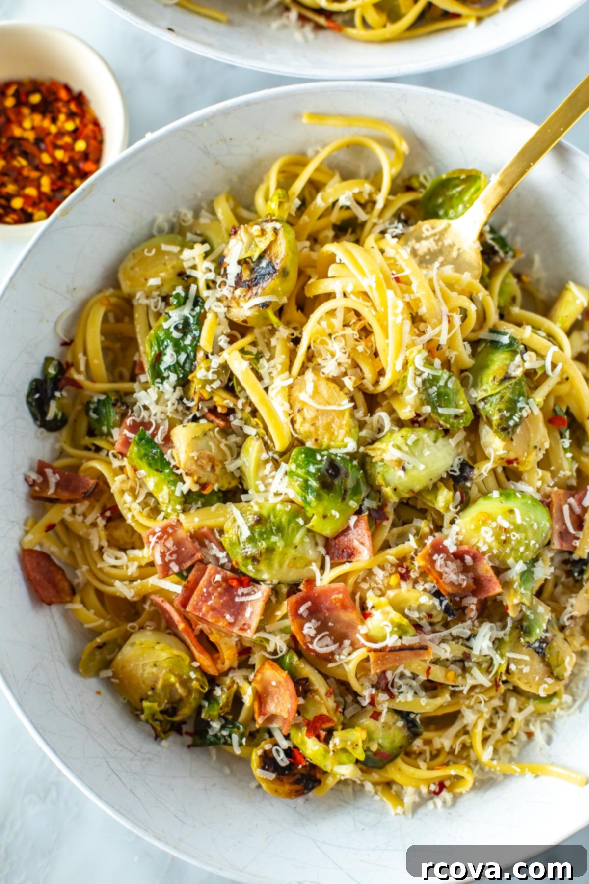 Bacon Brussels Sprouts Creamy Pasta 7 Another close-up of a generous serving of creamy brussels sprouts pasta in a white bowl, featuring visible pieces of crispy bacon, bright green brussels sprouts, and a hint of red chili flakes for color and spice, making it visually appealing.