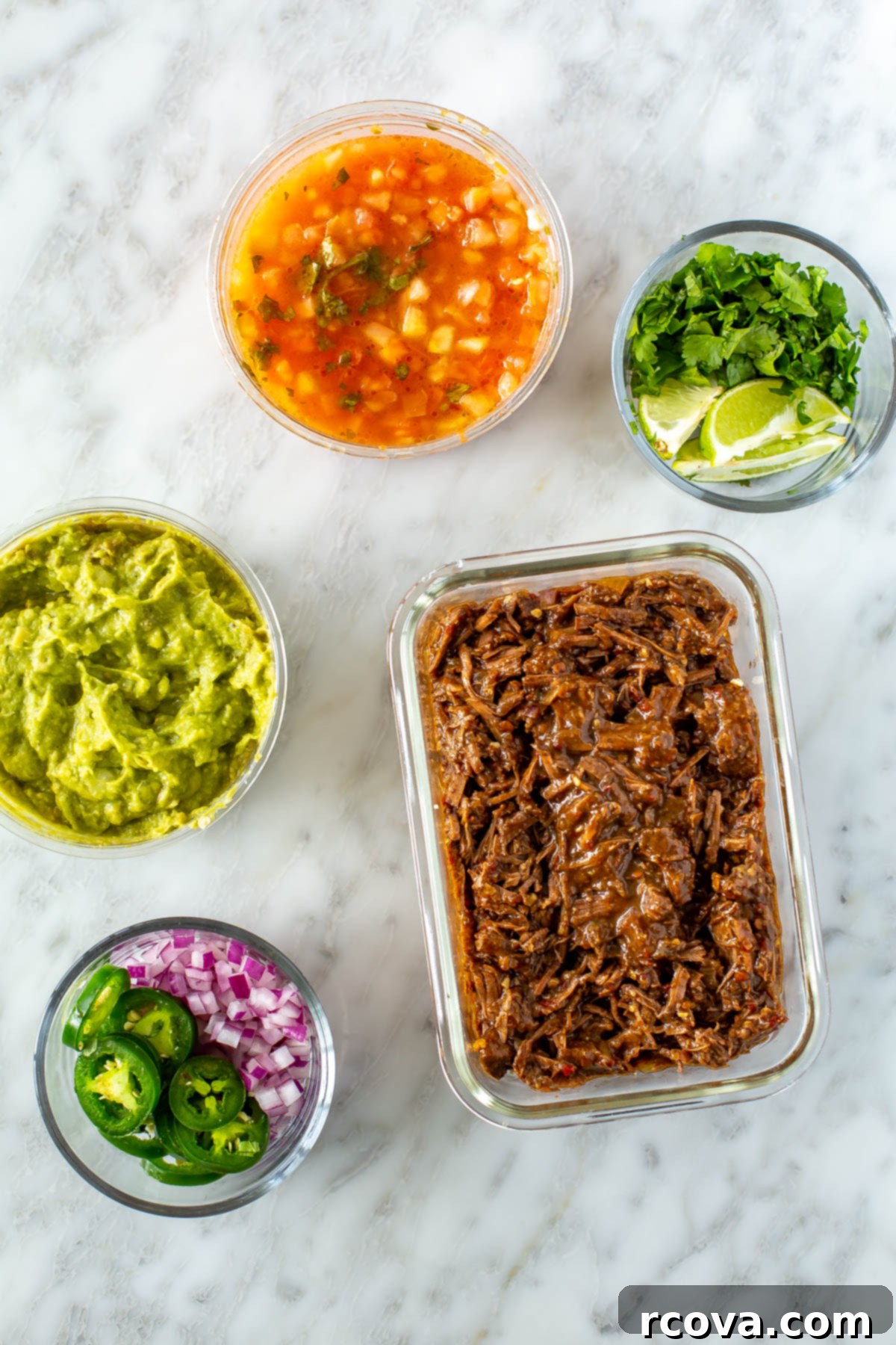 Crockpot Stovetop or Instant Pot Shredded Beef Tacos 10 Meal prep containers filled with shredded beef, pico de gallo, guacamole, cilantro and lime wedges and jalapeno and red onion.