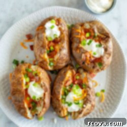 The Ultimate Fully Loaded Air Fryer Baked Potato 10 Four air fryer baked potatoes on a plate loaded with bacon, cheese, green onions, and sour cream, highlighting the rich textures.