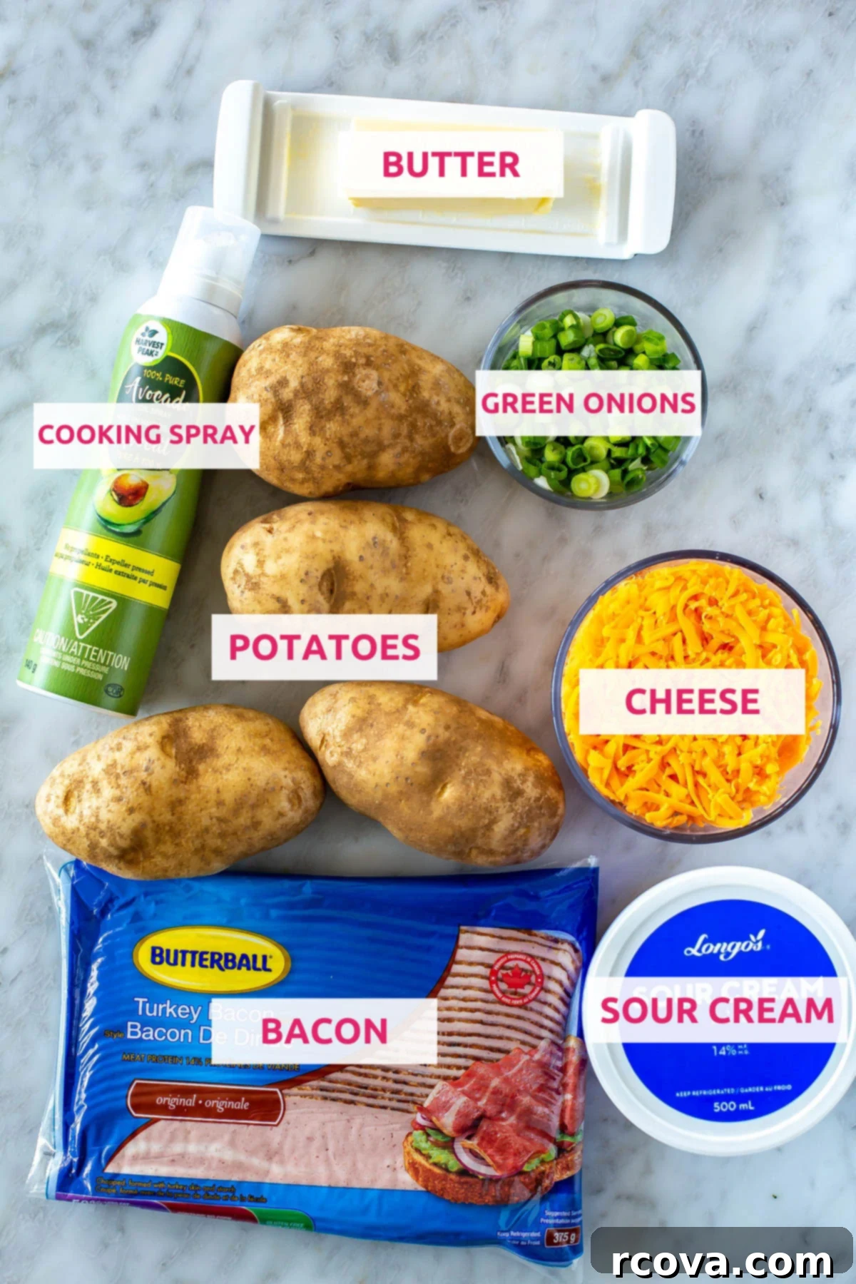 The Ultimate Fully Loaded Air Fryer Baked Potato 4 Ingredients for air fryer baked potatoes laid out: russet potatoes, butter, cooking spray, fresh green onions, shredded cheddar cheese, cooked bacon, and a bowl of sour cream.