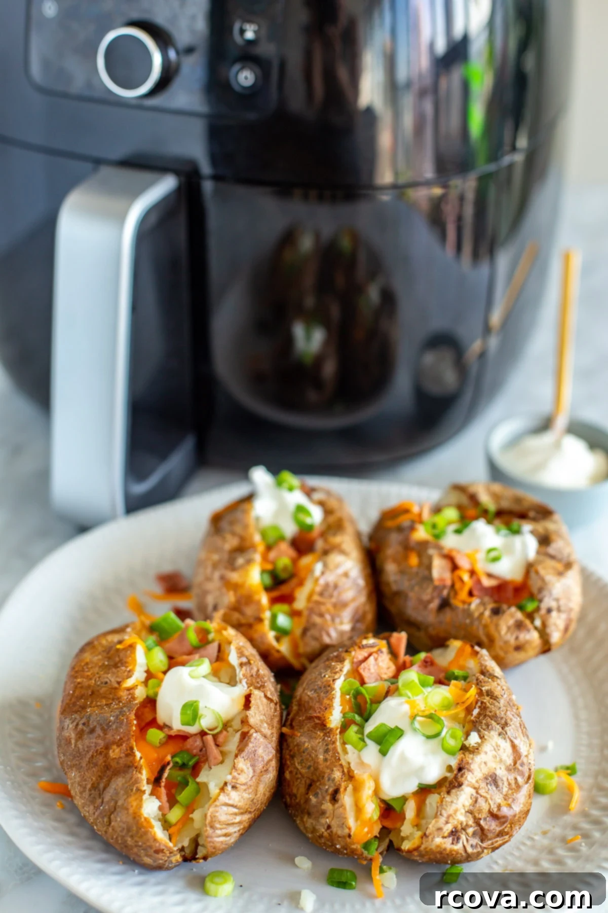 The Ultimate Fully Loaded Air Fryer Baked Potato 7 A plate of four fully loaded air fryer baked potatoes, with a visible air fryer in the soft focus background, emphasizing the convenience.
