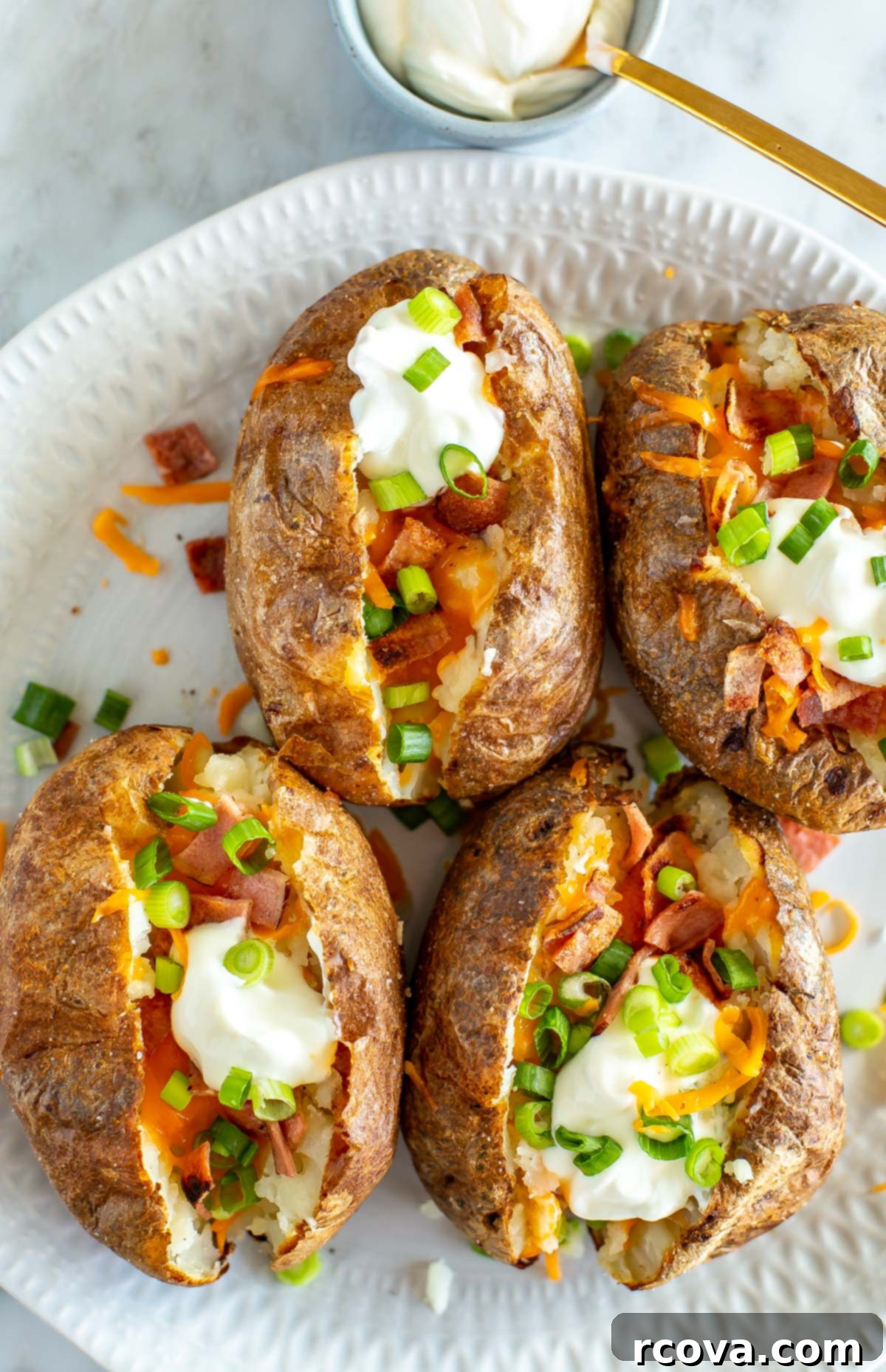 The Ultimate Fully Loaded Air Fryer Baked Potato 8 A close-up shot of four fully loaded air fryer baked potatoes, highlighting the rich textures of cheese, bacon, and sour cream on the crispy potato skin.