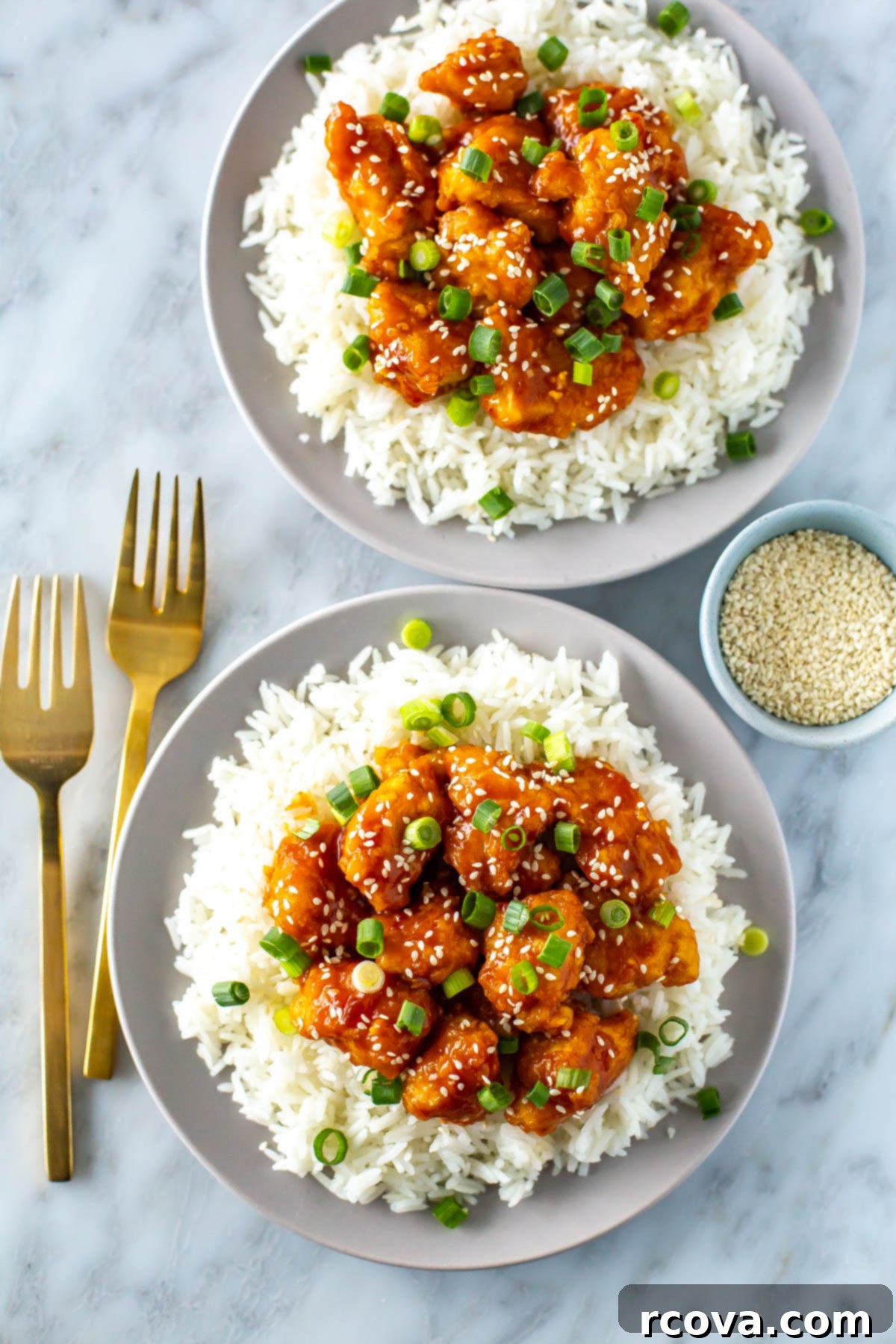 Quick Mandarin Chicken Delight 2 Two plates, each with a generous bed of jasmine rice, topped with golden-brown crispy Mandarin chicken and garnished with fresh green onions and sesame seeds.