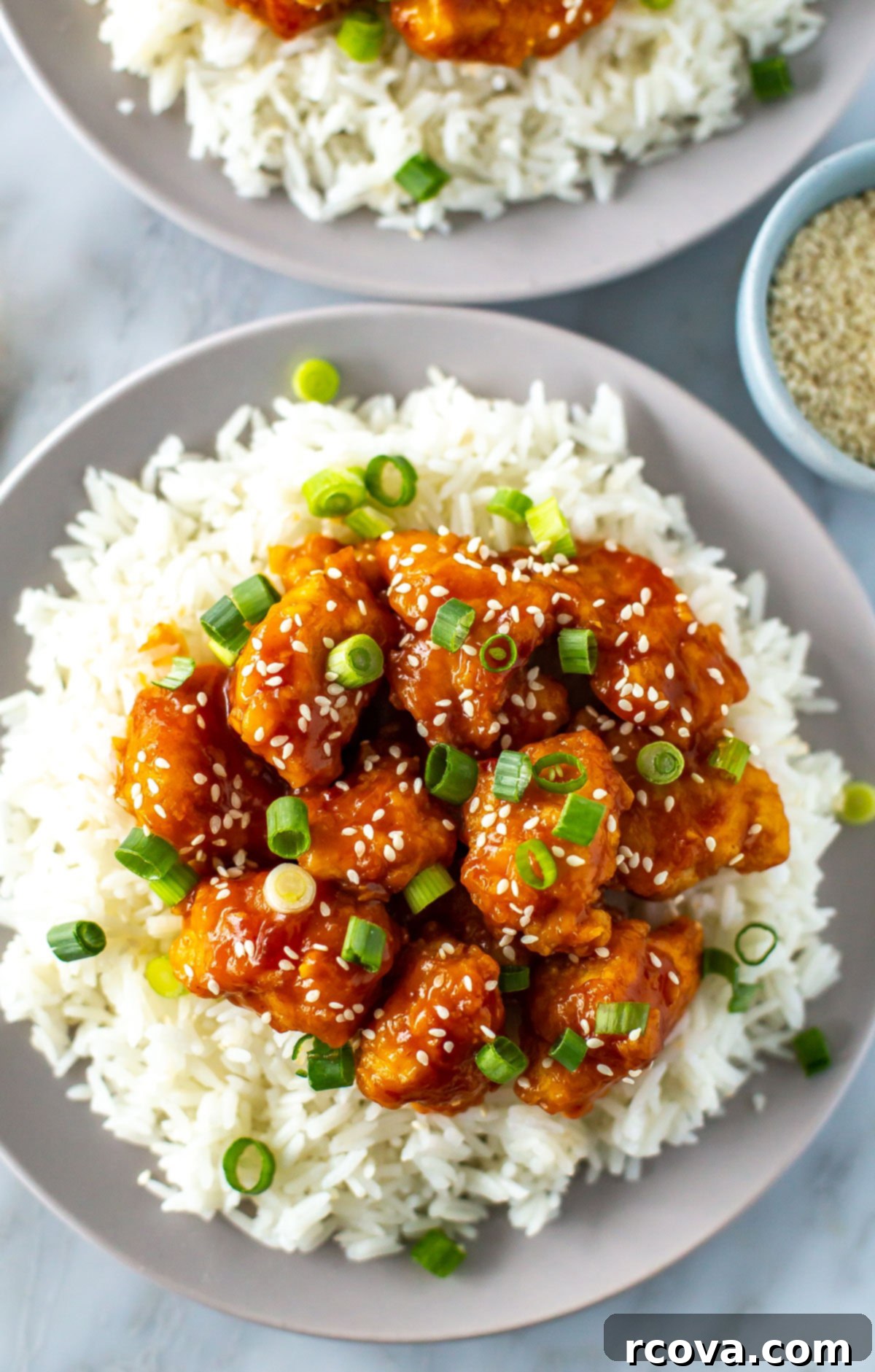 Quick Mandarin Chicken Delight 9 A high-angle close-up of a plate of crispy Mandarin chicken, glistening with orange sauce, served on rice with fresh green onions and sesame seeds.