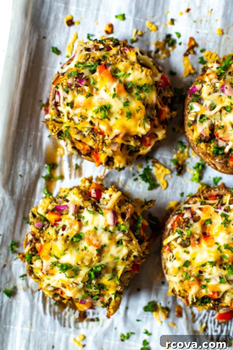 Deliciously Healthy Mushroom Recipes 4 Stuffed portobello mushrooms on a sheet pan lined with parchment paper, filled with chicken, breadcrumbs, cheese, and red pepper.