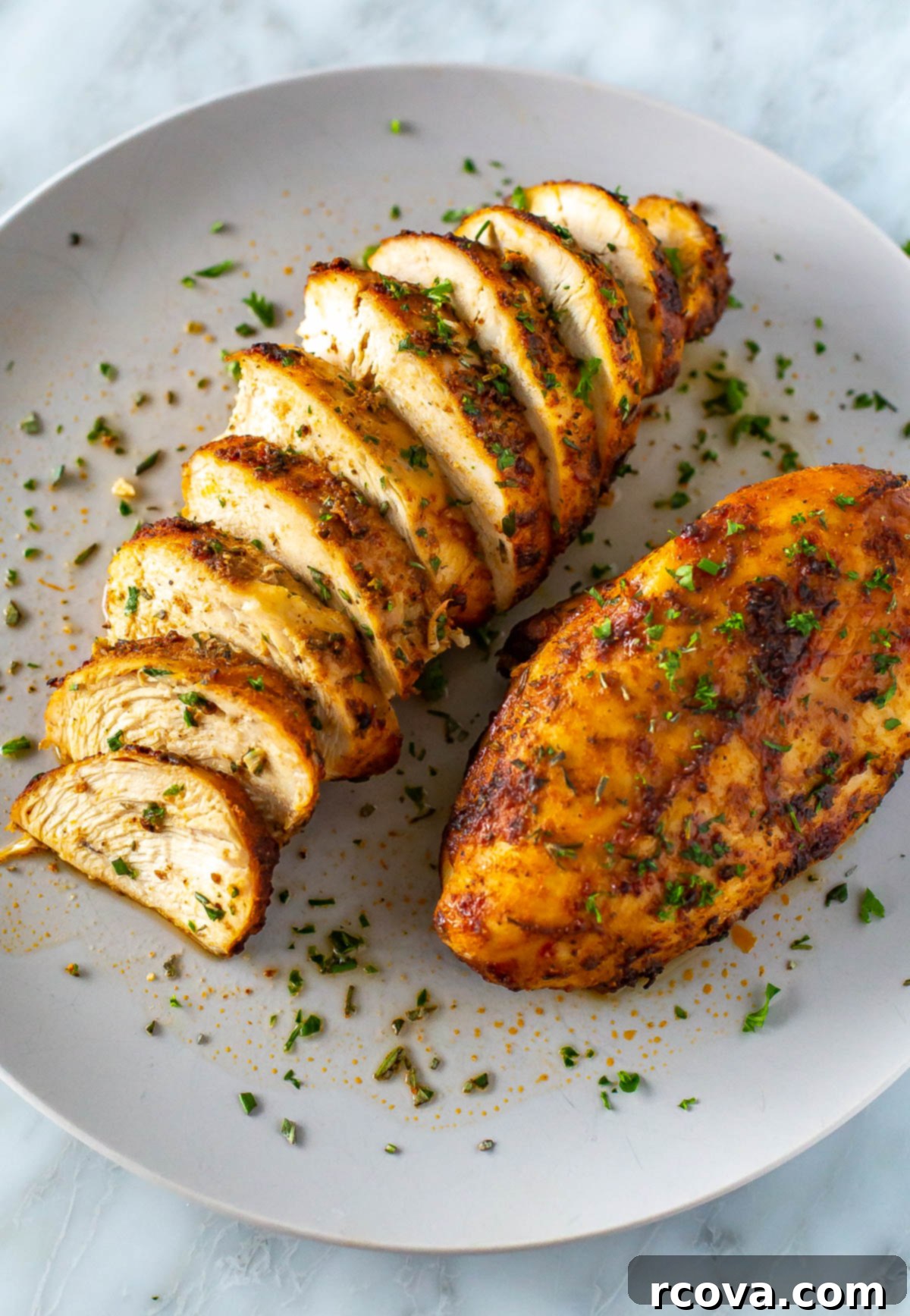 Perfect Air Fryer Chicken Breasts The Ultimate Marinade 2 A plate with one whole air fryer chicken breast and another one that has been sliced, showcasing its juicy interior.