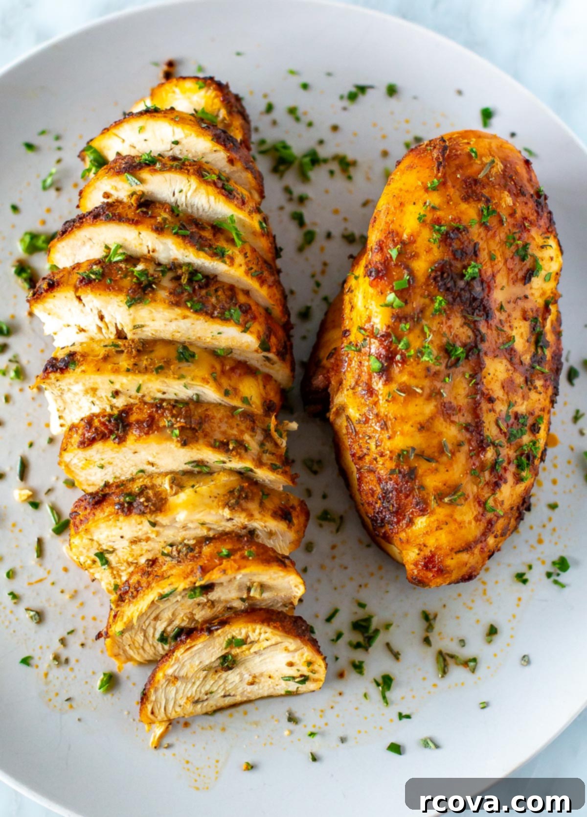Perfect Air Fryer Chicken Breasts The Ultimate Marinade 9 A close-up of a plate with one whole air fryer chicken breast and another one that has been sliced, highlighting the perfect texture.