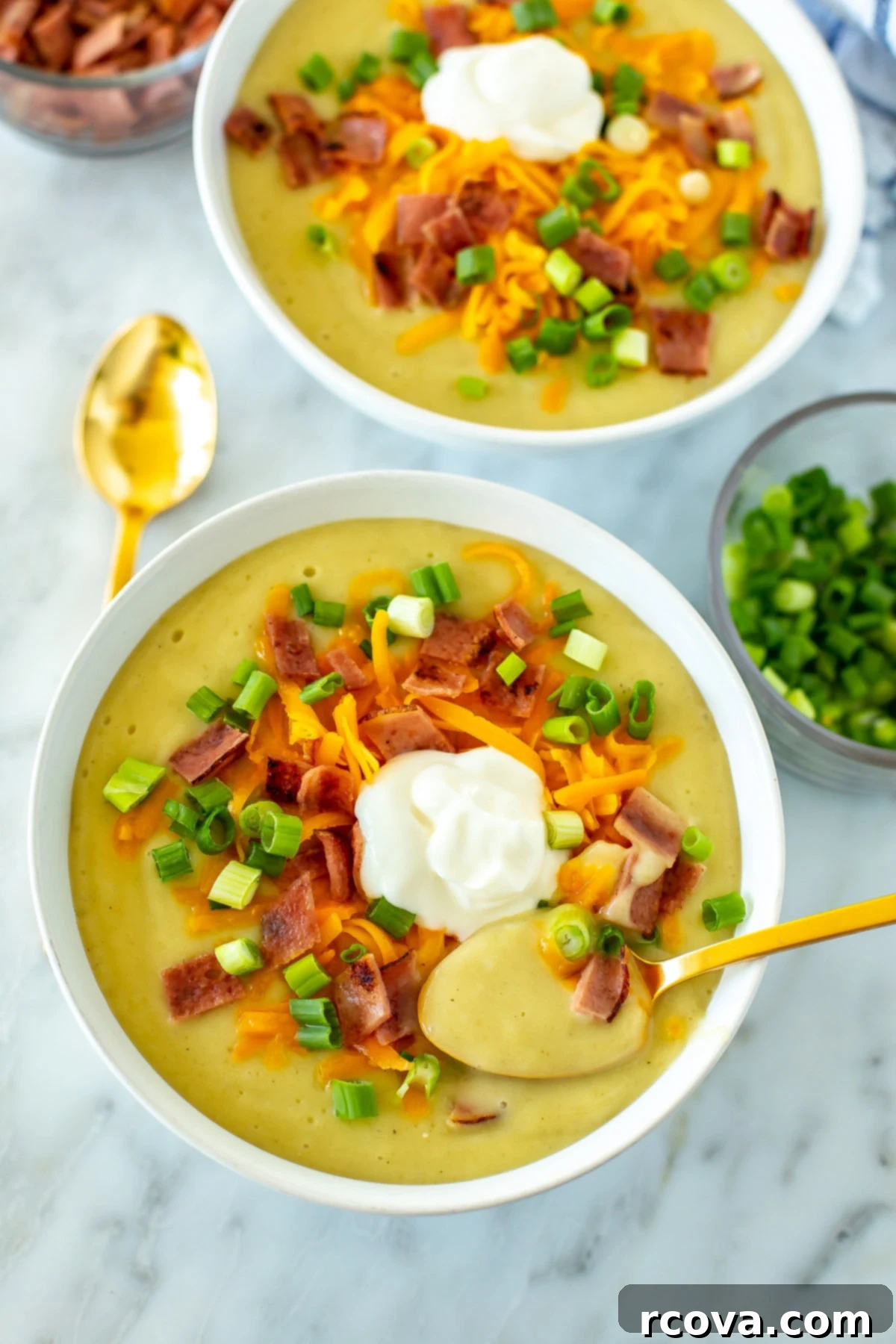 20 No-Fuss Slow Cooker Soup Recipes 17 Two creamy bowls of crockpot potato soup, topped with chives, with a spoon resting in the foreground.