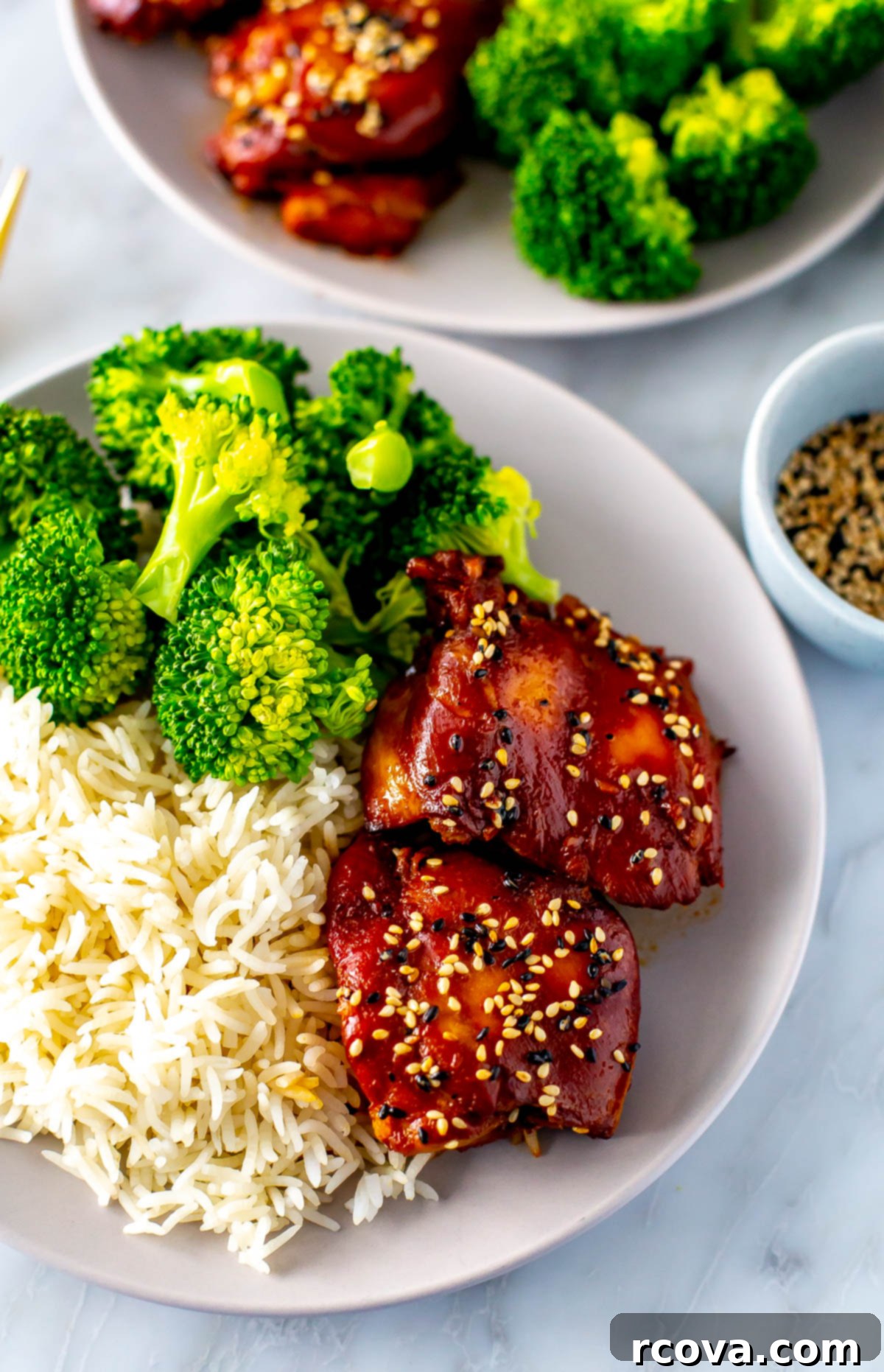 Honey Garlic Slow Cooker Chicken 10 Another perspective of a plate of slow cooker honey garlic chicken thighs served with broccoli and rice, garnished with green onions and sesame seeds.