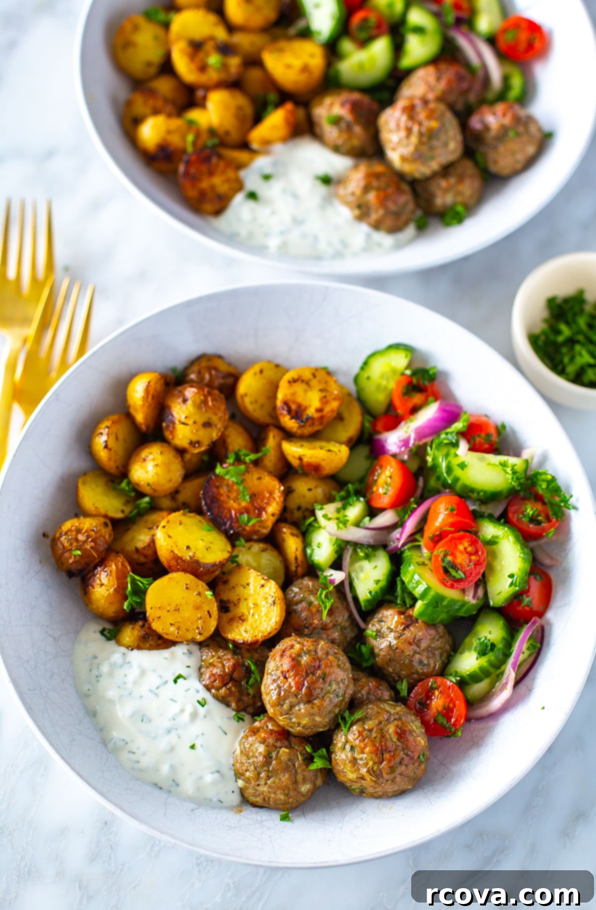 Oven-Roasted Greek Meatballs and Tangy Tzatziki 9 A close-up of a bowl of greek chicken meatballs with a side of potatoes, veggies and tzatziki.