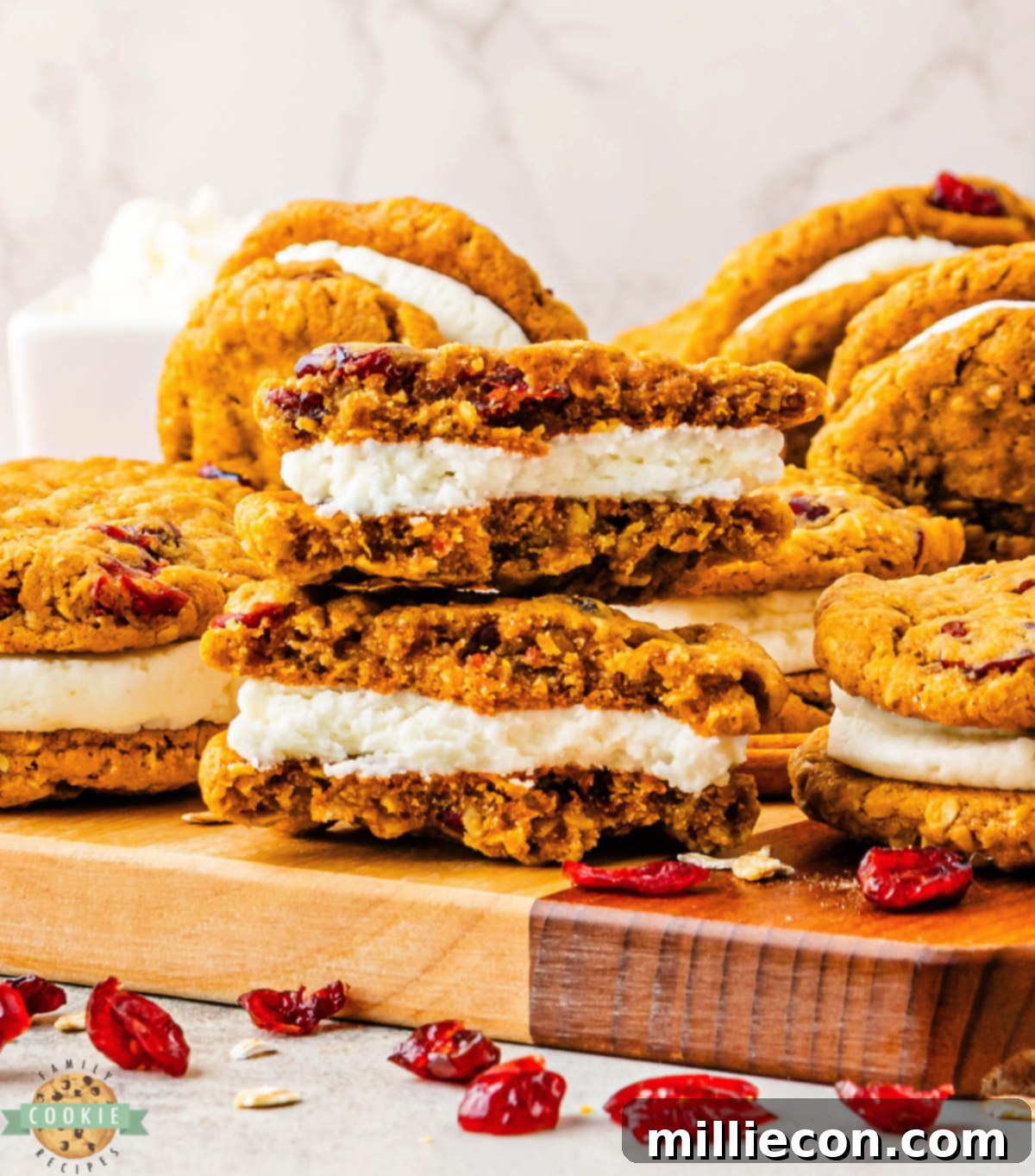 Spiced Pumpkin Cranberry Oatmeal Sandwich Cookies 9 Soft pumpkin oatmeal cookies with dried cranberries and creamy frosting filling stacked on a wooden cutting board.