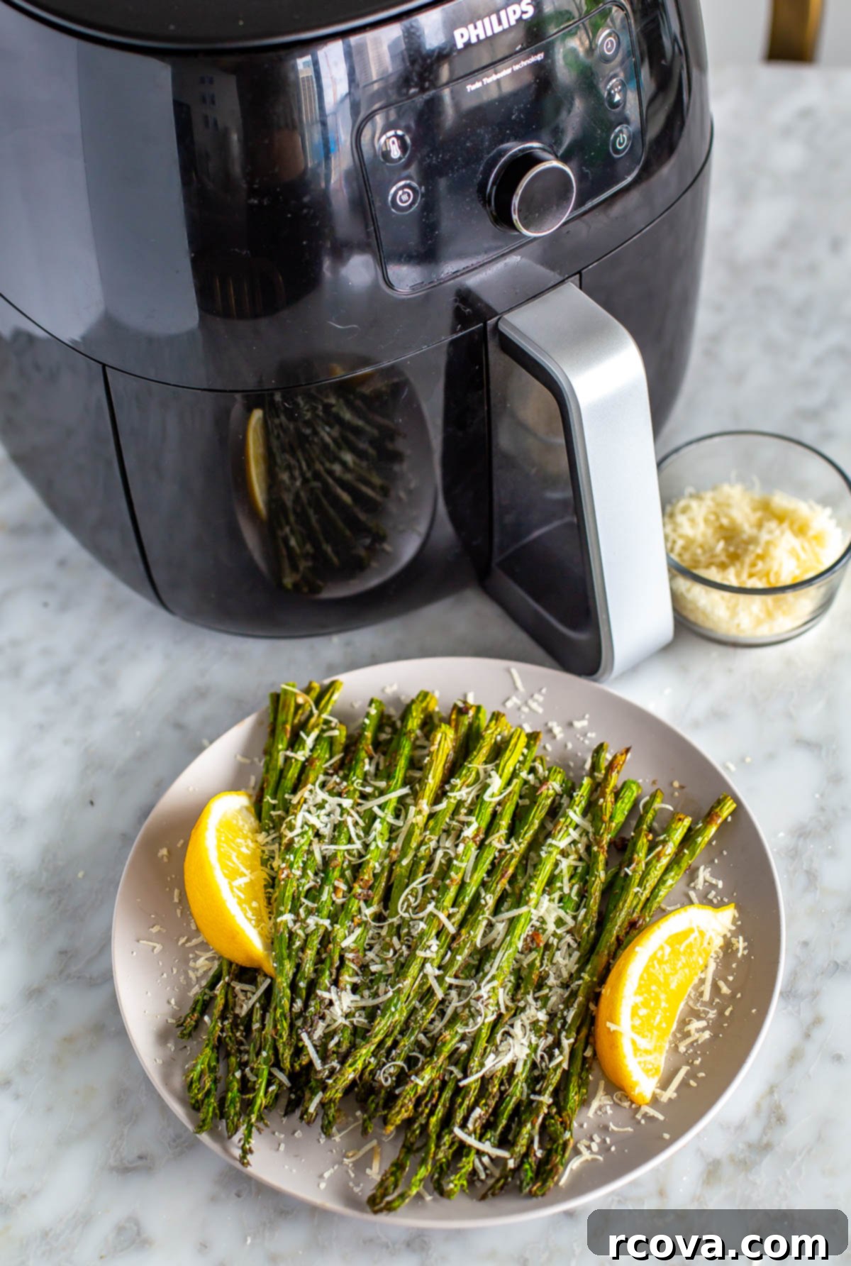 Crispy Air Fryer Asparagus 7 An air fryer in the background with a plate of garlic parm air fryer asparagus in the foreground, showcasing its crispy texture.
