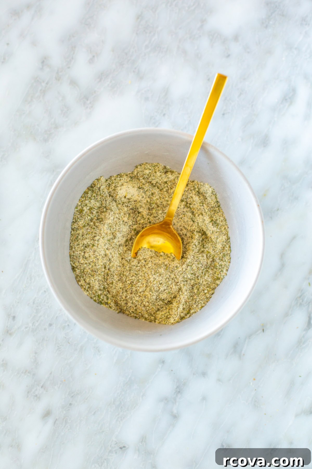 Foolproof Homemade Ranch Mix 6 A close-up shot of homemade ranch seasoning being stirred in a bowl with a spoon, highlighting its fresh texture and vibrant herb flecks.