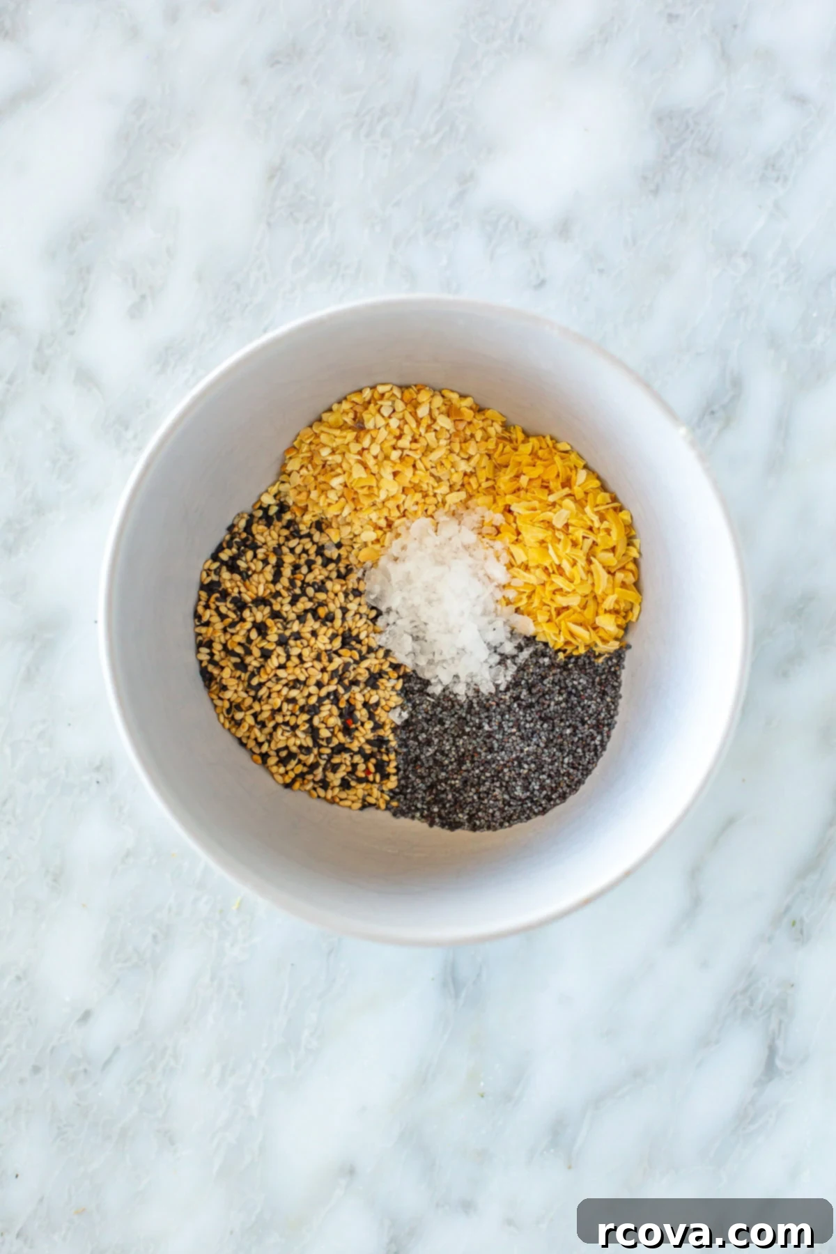 Everything Bagel Seasoning That Outperforms TJs 2 Bowl of various spices, including black and white sesame seeds, poppy seeds, dried minced garlic, and dried minced onion, ready to be mixed into homemade everything bagel seasoning. A spoon rests in the bowl.