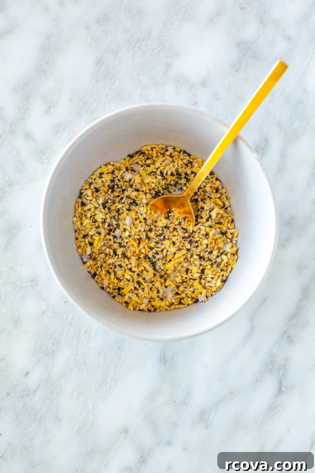 Everything Bagel Seasoning That Outperforms TJs 6 A close-up shot of homemade everything bagel seasoning mixed in a bowl with a small wooden spoon, showcasing its rich texture and distinct ingredients.
