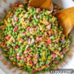 Creamy Pea Salad Perfection 9 Creamy pea salad in a large salad bowls with two wooden tongs in it.