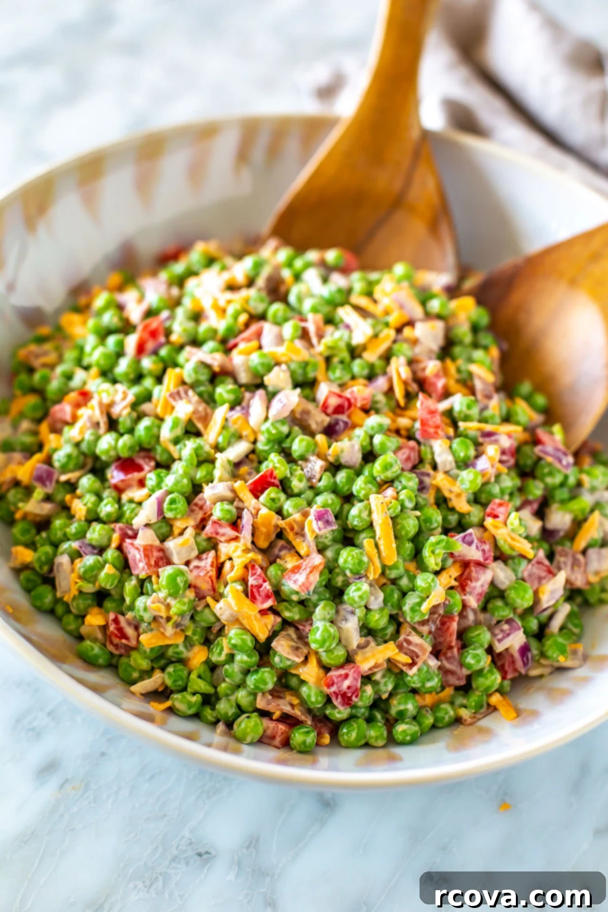 Creamy Pea Salad Perfection 6 Creamy pea salad in a large salad bowls with two wooden tongs in it.