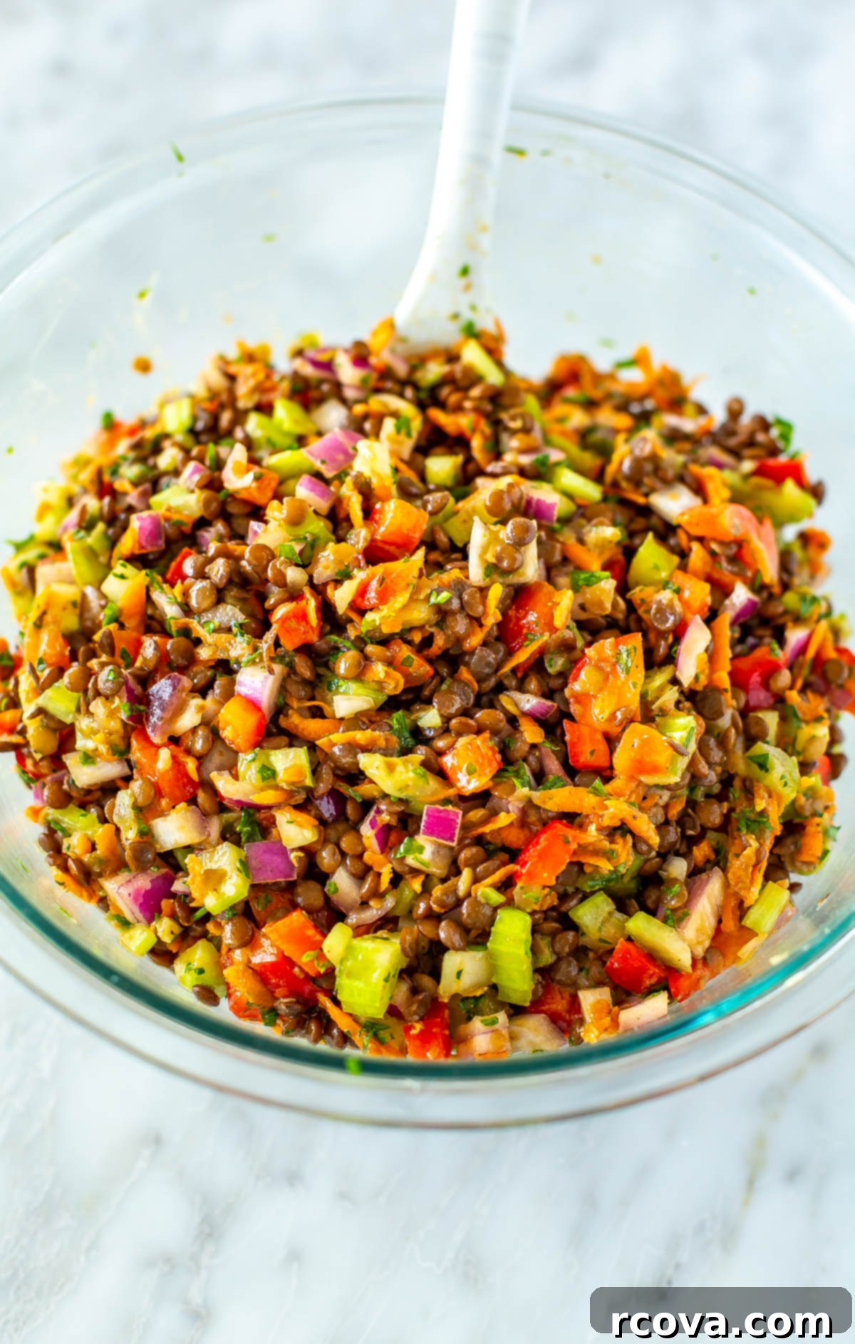 The Ultimate Lentil Salad Recipe 8 A large, clear glass bowl overflowing with a colorful and appetizing lentil salad, ready to be served.