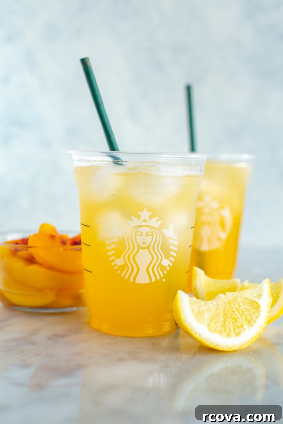 Make Your Own Starbucks Summer Drinks At Home 11 Two cups of homemade Starbucks iced peach green tea lemonade with peach slices.