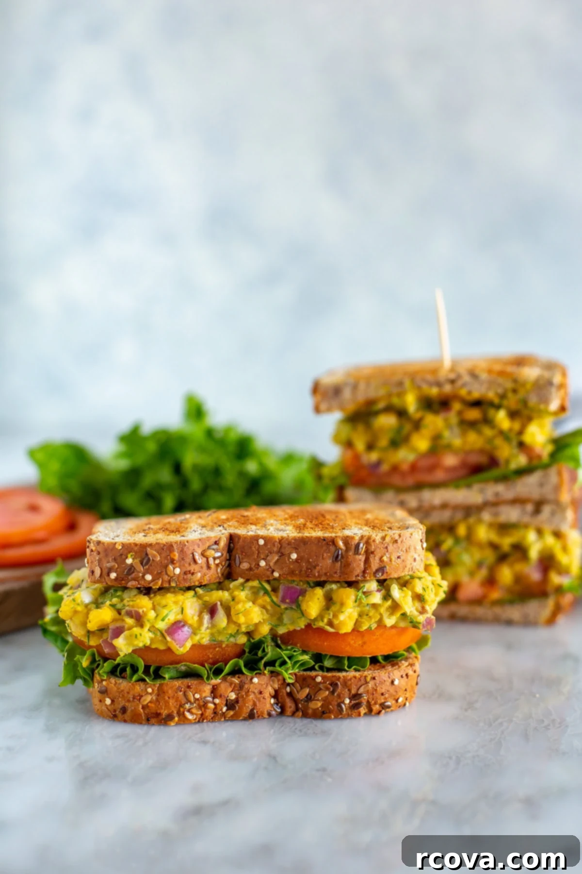 Chickpea Tuna Salad Sandwich: A Vegetarian Delight 8 A chickpea tuna salad sandwich in the foreground with two in the background, showing the appealing texture and fresh garnishes.