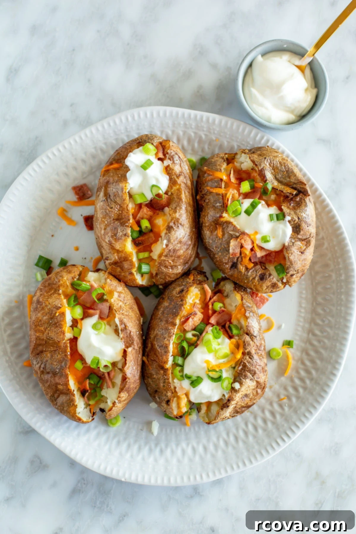 Effortless & Flavorful: 18 Air Fryer Delights 18 Four air fryer baked potatoes on a plate loaded with bacon, cheese, green onions, and sour cream.