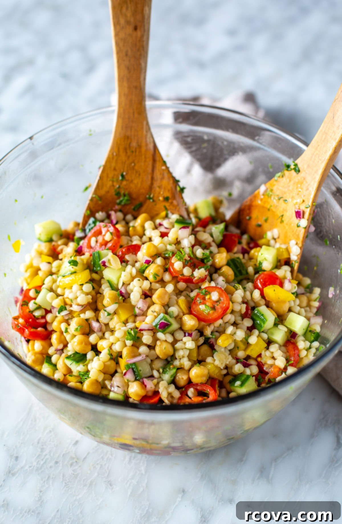 Effortless Mediterranean Couscous Salad for Meal Prep 6 A large bowl filled with colorful Mediterranean couscous salad, featuring two wooden salad servers.