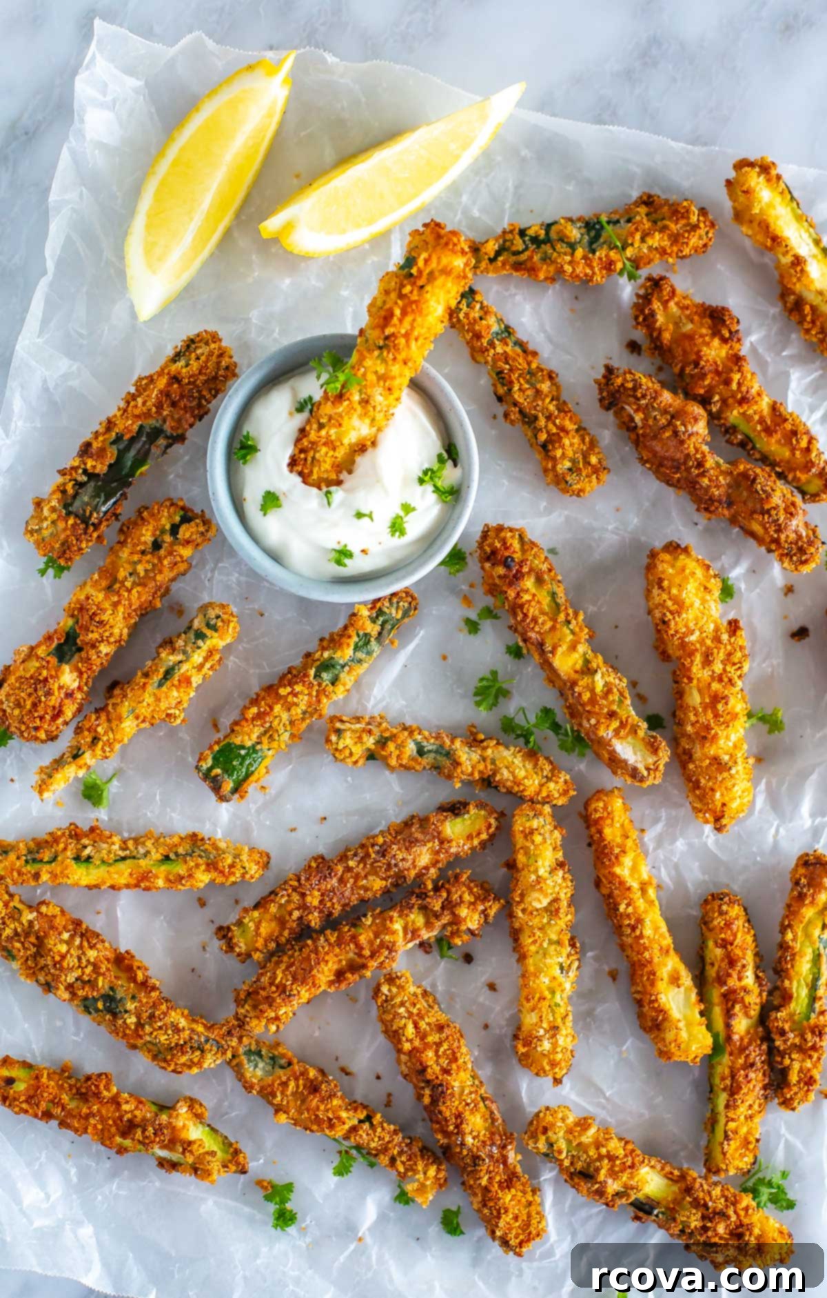 Perfectly Crispy Air Fryer Zucchini Fries 8 Multiple air fryer zucchini fries on a piece of parchment paper with one being dipped in garlic aioli.