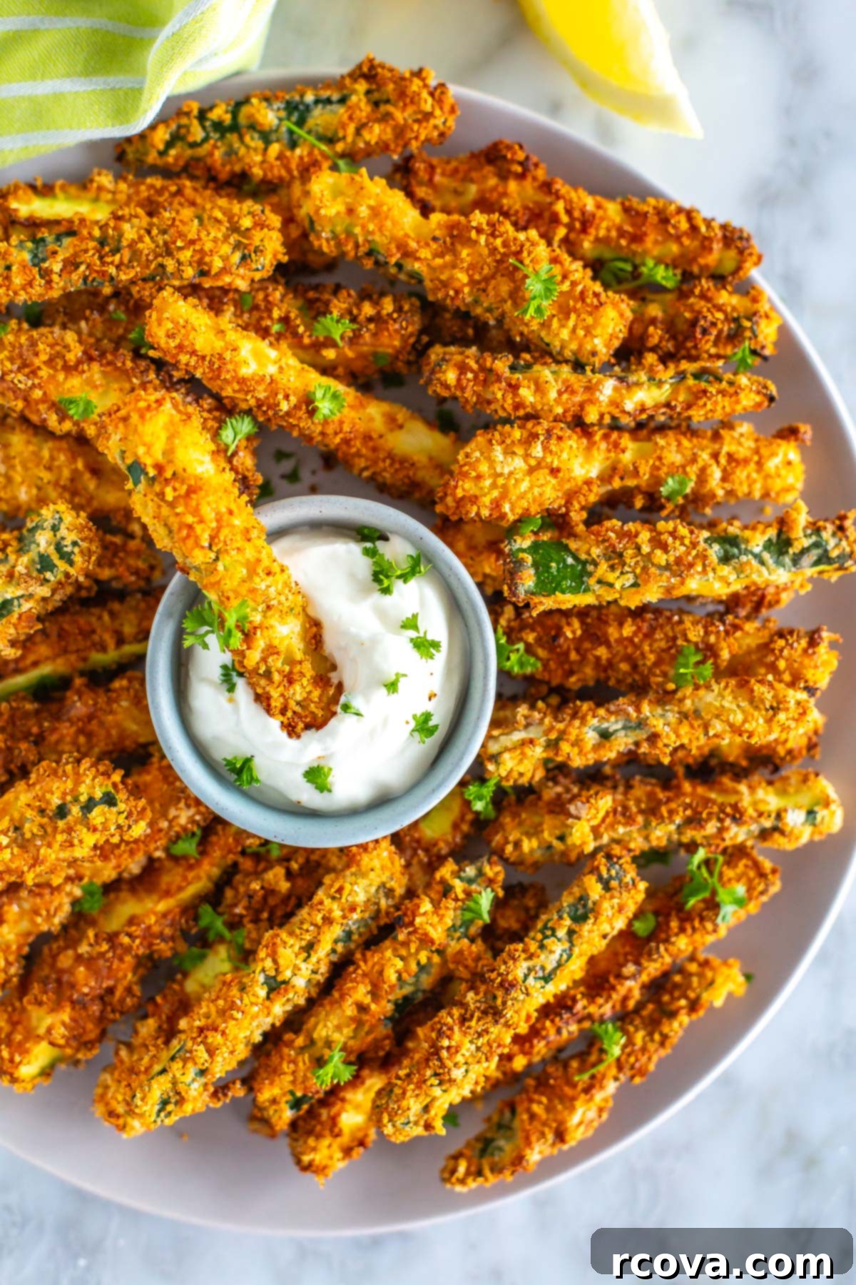 Perfectly Crispy Air Fryer Zucchini Fries 9 A close-up of a plate of air fryer zucchini fries, with one being dipped in garlic aioli.