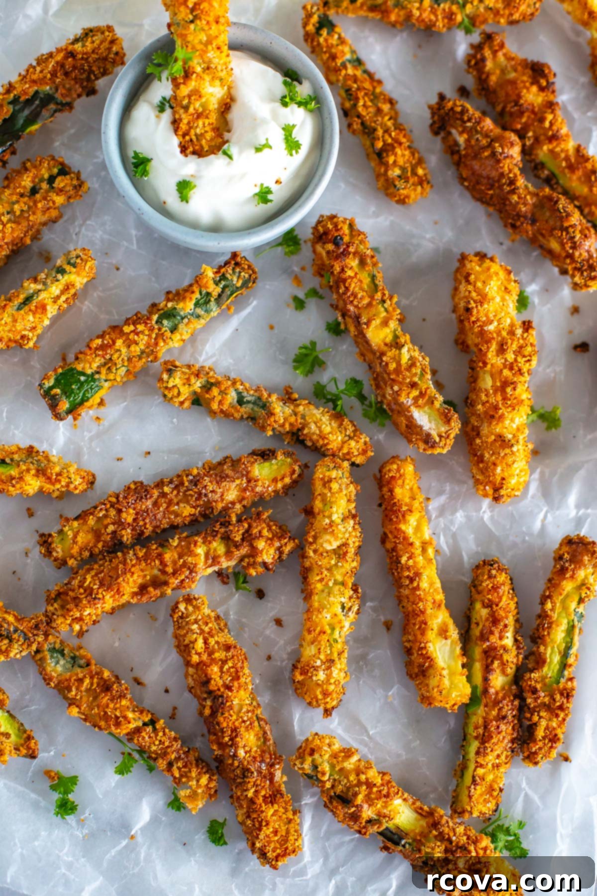 Perfectly Crispy Air Fryer Zucchini Fries 10 Multiple air fryer zucchini fries on a sheet of parchment paper, with one being dipped into garlic aioli.