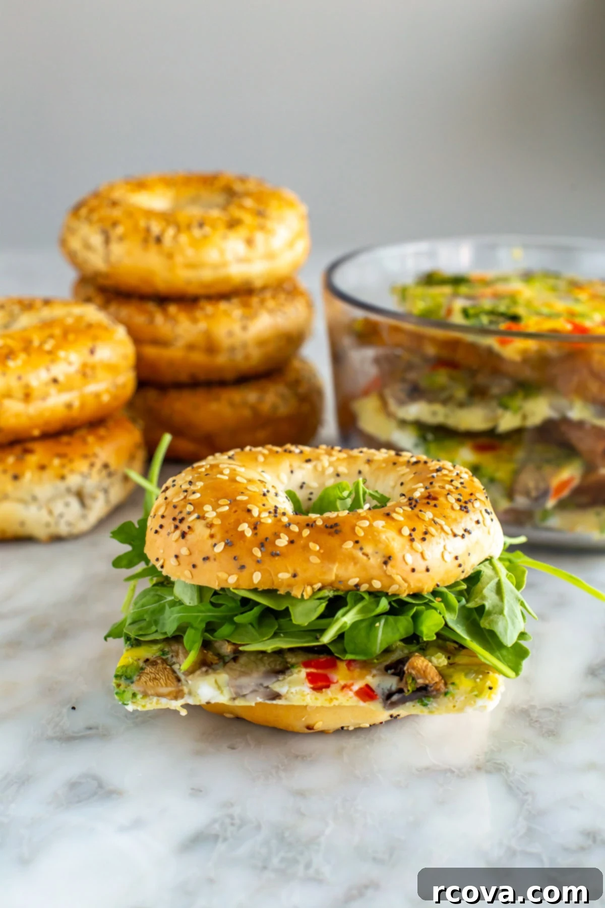 Big Batch Sheet Pan Eggs 8 A perfectly assembled breakfast sandwich featuring a square of sheet pan egg with melted cheese, fresh arugula, and crispy bacon, nestled inside a toasted bagel.