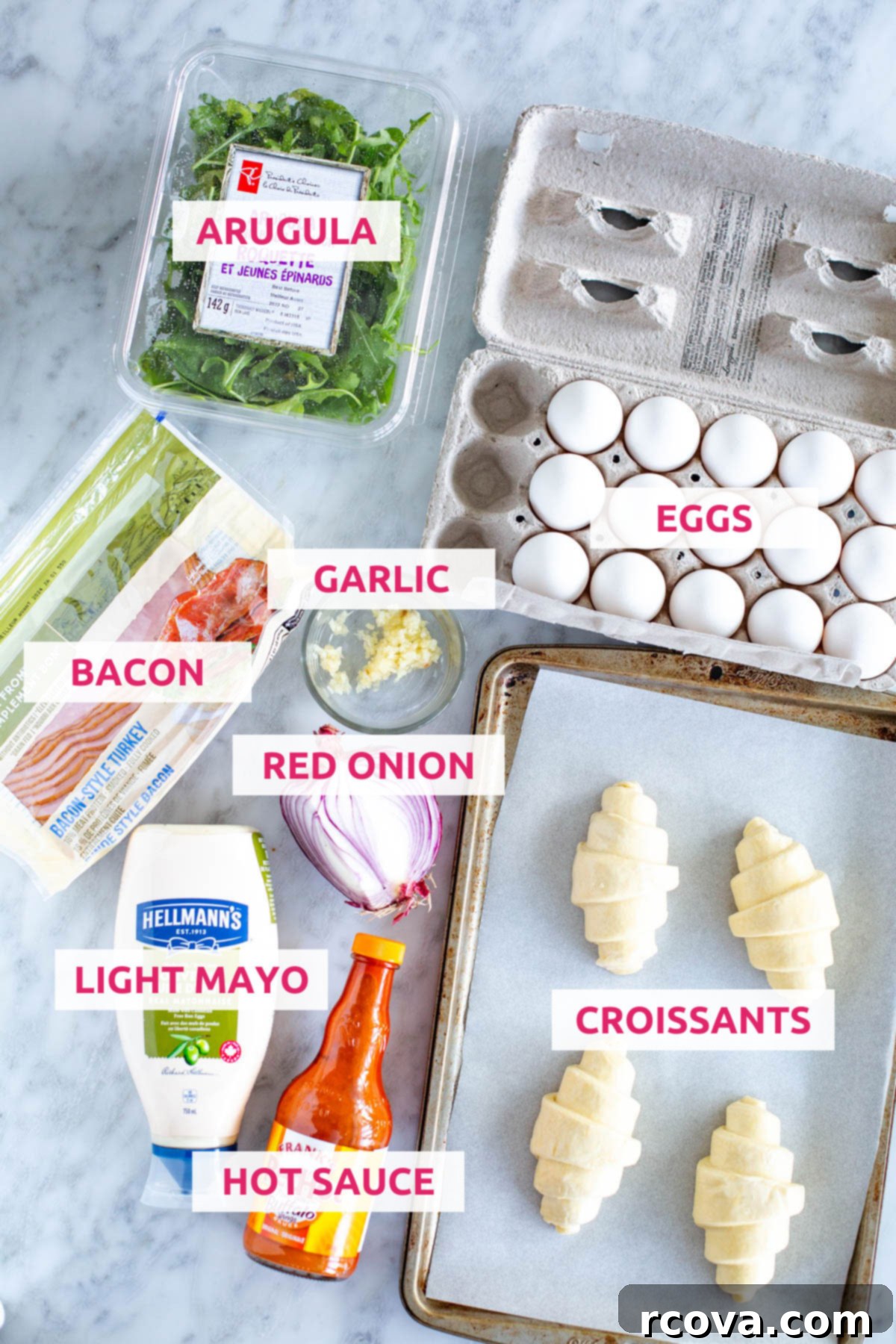 Ready-to-Go Croissant Breakfast Sandwiches 4 A vibrant flat lay of ingredients for building the ultimate croissant breakfast sandwich: golden croissants, fresh eggs, crisp arugula, perfectly cooked bacon, pungent garlic, your favorite hot sauce, creamy light mayo, and thinly sliced red onion.