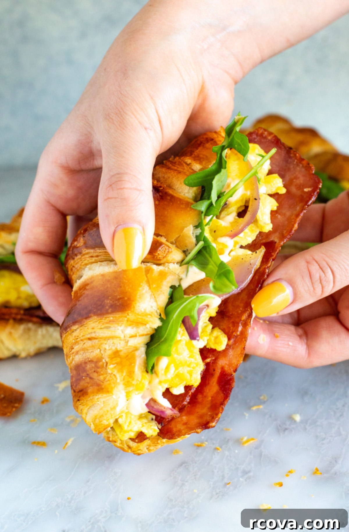 Ready-to-Go Croissant Breakfast Sandwiches 9 A hand gracefully holds a perfectly assembled croissant breakfast sandwich, showcasing the golden-brown pastry and the inviting layers of filling, ready for a delicious bite.