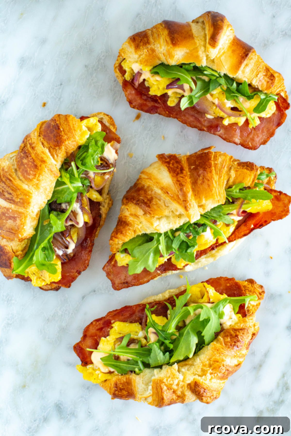 Ready-to-Go Croissant Breakfast Sandwiches 10 Four perfectly portioned make-ahead croissant breakfast sandwiches, displaying their delectable fillings of crispy bacon, scrambled eggs, and fresh arugula, artfully arranged and ready to be enjoyed.