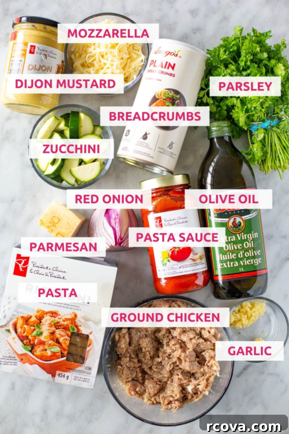 Cheesy Chicken Parmesan Meatballs 4 Ingredients for chicken parmesan meatballs laid out: Dijon mustard, shredded mozzarella, breadcrumbs, fresh parsley, sliced zucchini, red onion, pasta sauce, olive oil, parmesan cheese, dry pasta, ground chicken, and minced garlic.