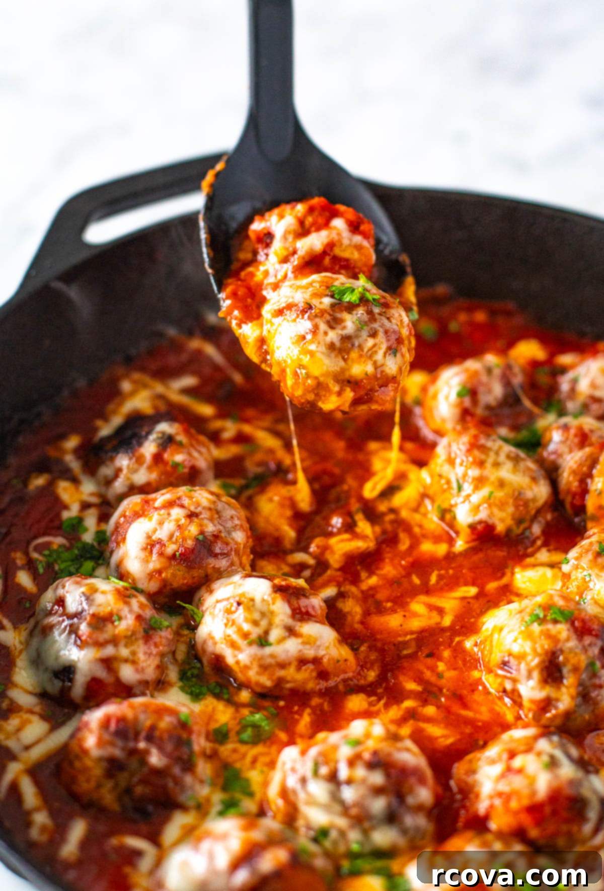 Cheesy Chicken Parmesan Meatballs 8 A single chicken parmesan meatball being lifted from a skillet with tongs, showcasing its cheesy topping.
