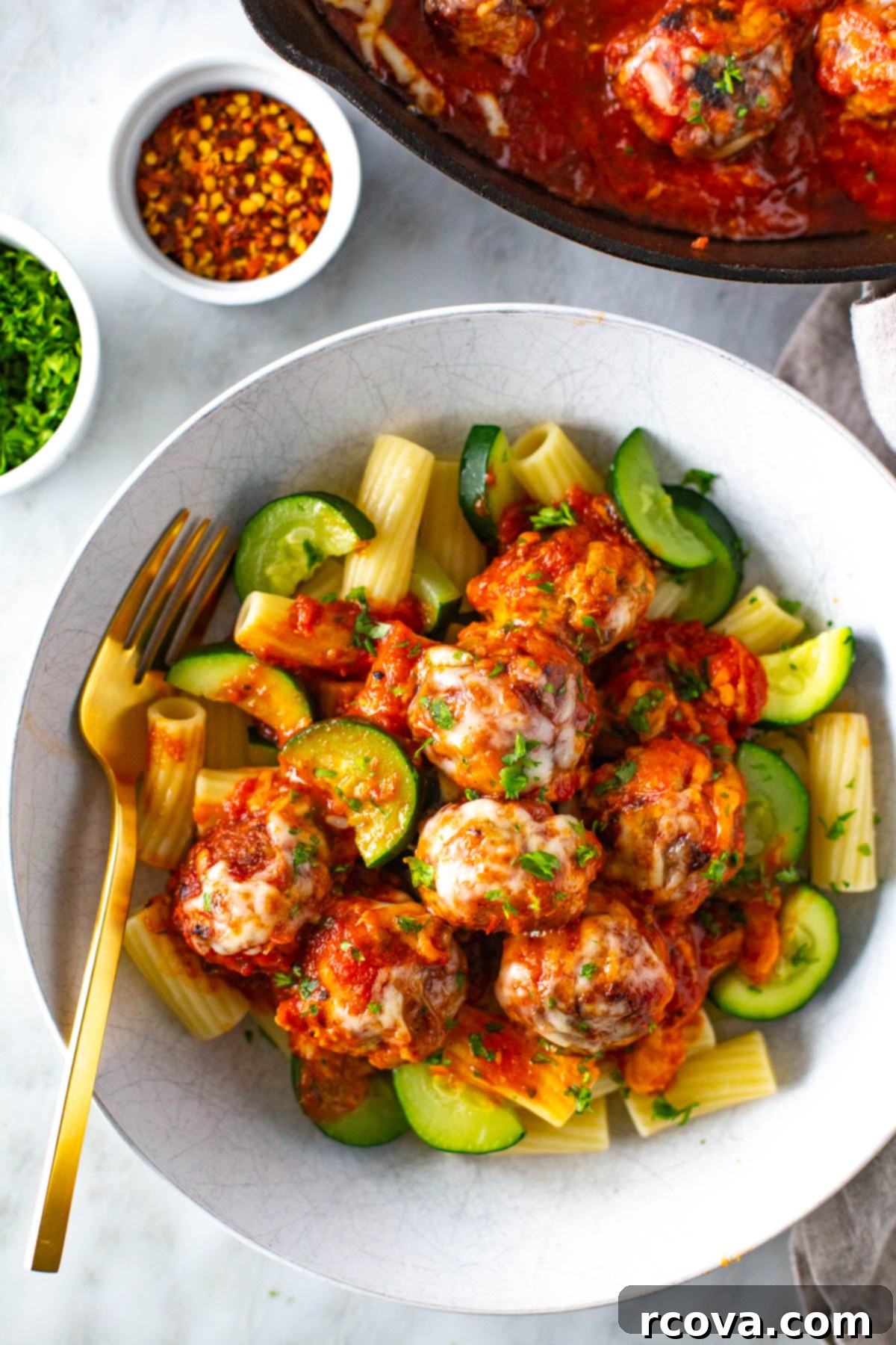 Cheesy Chicken Parmesan Meatballs 9 A close-up of chicken parmesan meatballs served alongside perfectly cooked pasta and vibrant green zucchini, garnished with fresh herbs.