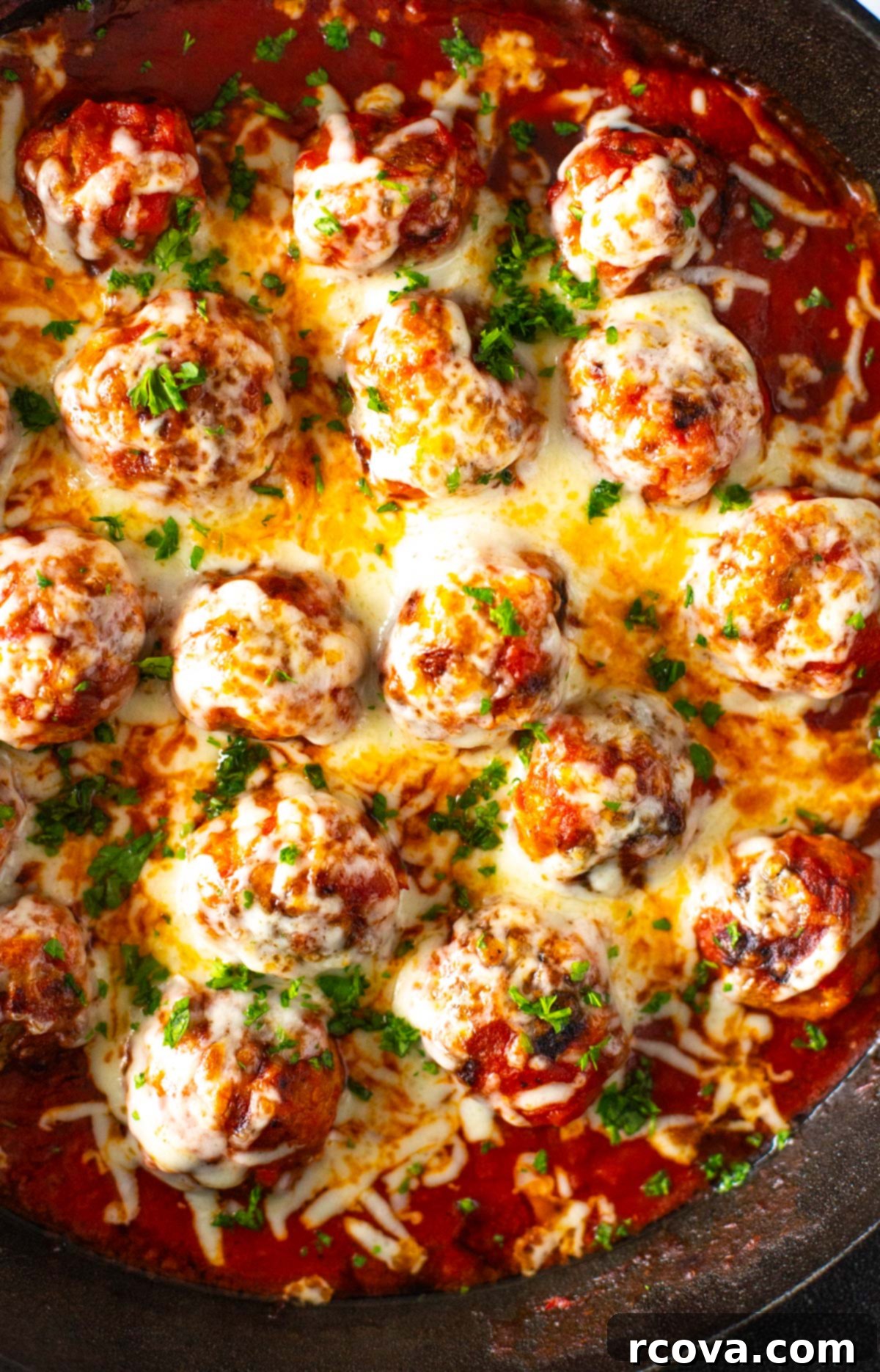 Cheesy Chicken Parmesan Meatballs 10 A close-up of beautifully browned chicken parm meatballs in a skillet, generously covered with melted, bubbly mozzarella cheese and a sprinkle of fresh green herbs.