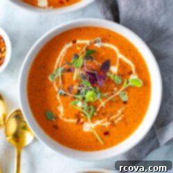 Smoky Red Pepper Bisque 10 A close-up of a bowl of roasted red pepper soup topped with heavy cream and microgreens.