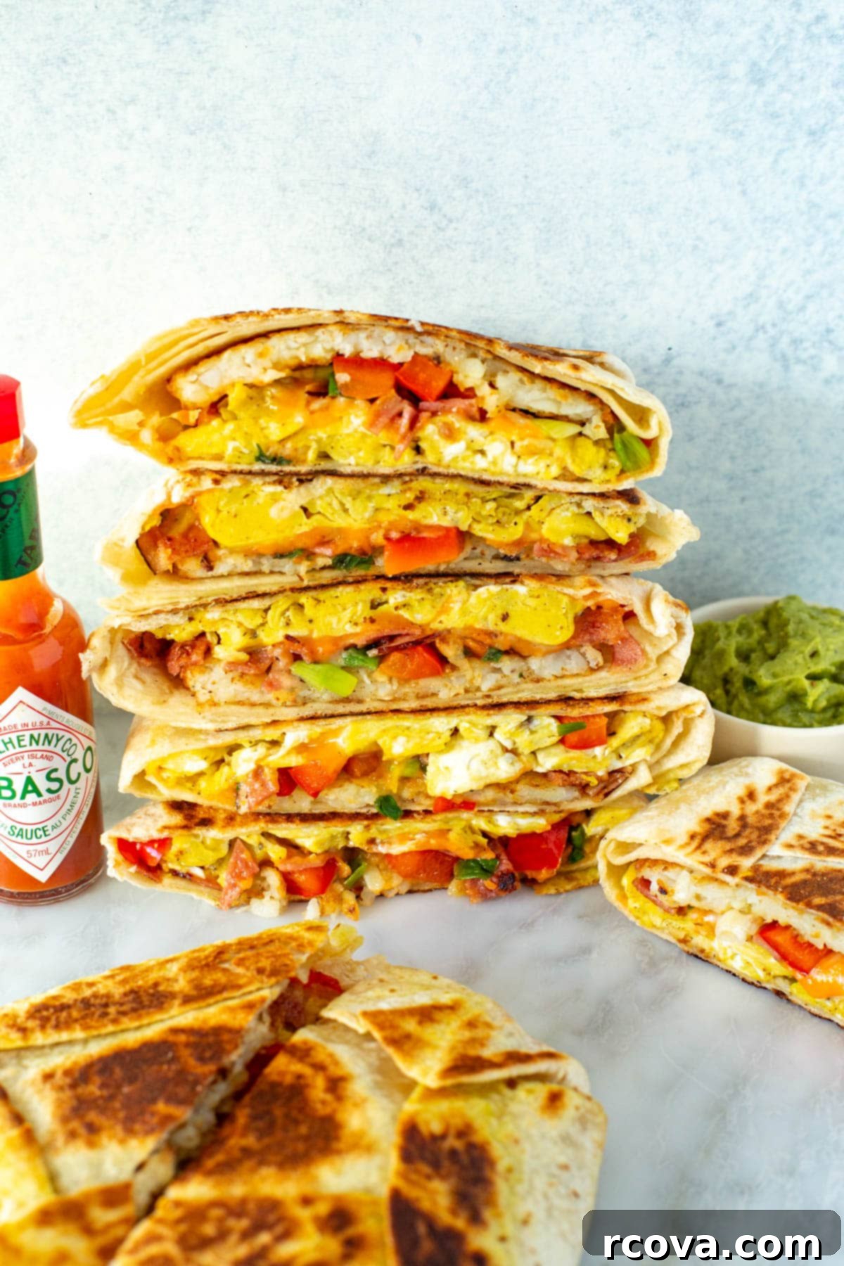 Mastering the Taco Bell Breakfast Crunchwrap at Home 9 Cut open breakfast crunchwraps stacked together with a side of hot sauce and guacamole