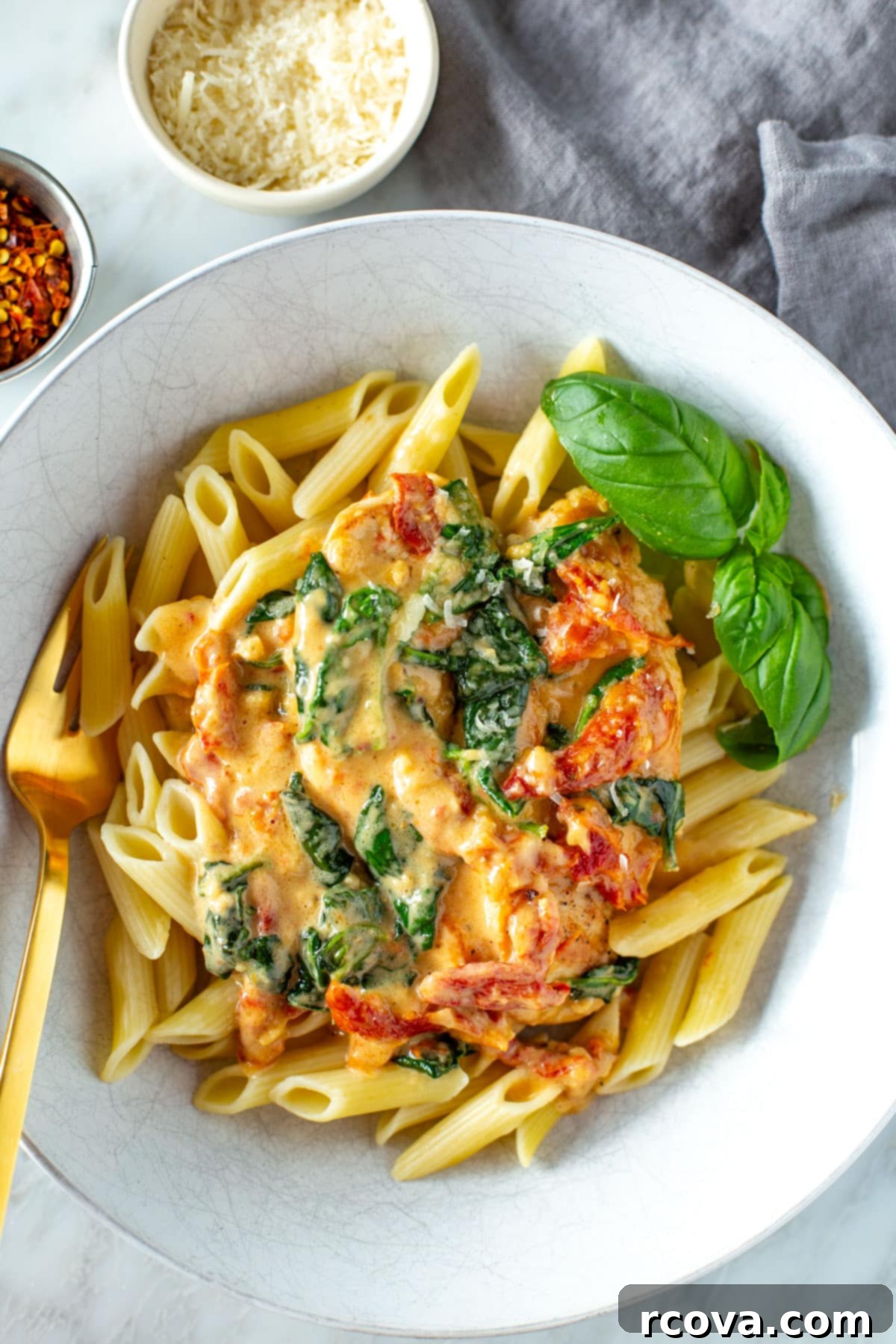 Luxurious Marry Me Chicken 9 Marry me chicken served over pasta and garnished with fresh basil, with grated parmesan and chili flakes on the side.
